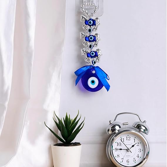Evil Eye Home Decor Charm in blue with silver accents and a decorative ribbon near a clock and plant
